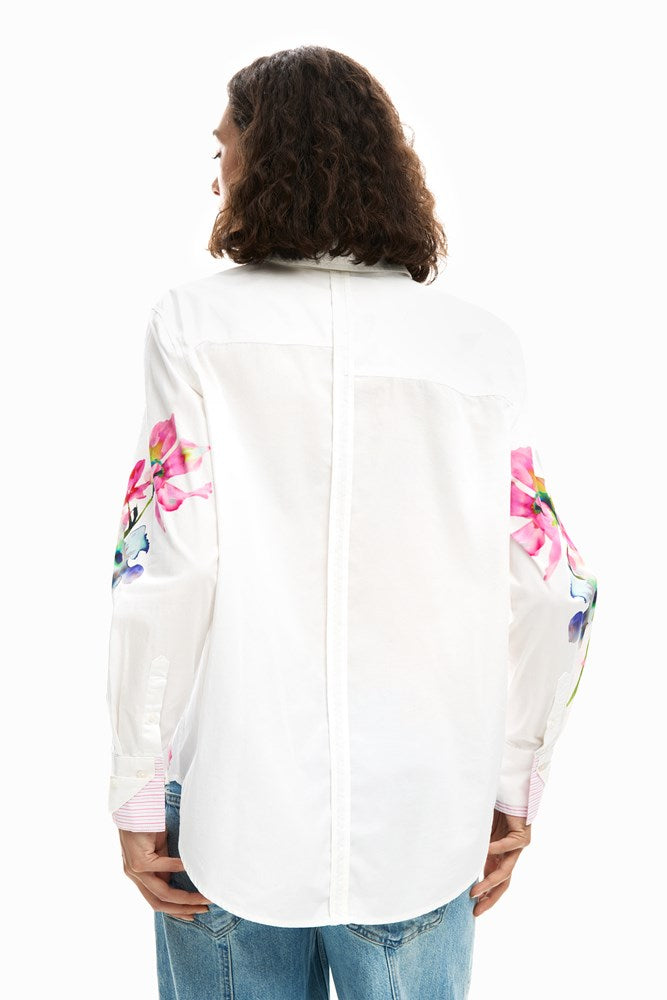 Person wearing a white shirt with colorful floral patterns on the sleeves against a white background