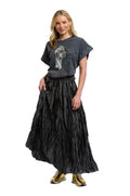 A woman modeling a dark gray graphic t-shirt and a long, crinkled black maxi skirt, paired with gold sneakers, against a plain white background.