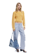 A woman modeling a yellow ribbed knit cropped sweater, light blue wide-leg cargo pants, and a blue denim shoulder bag against a plain white background.