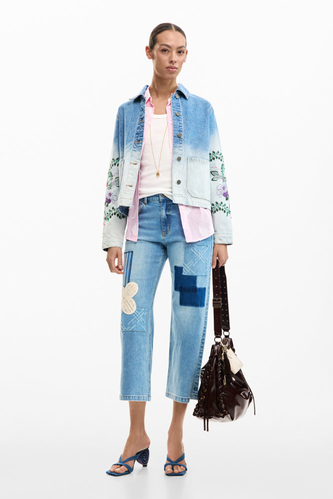 Woman wearing a colorful denim jacket and patchwork jeans on a white background