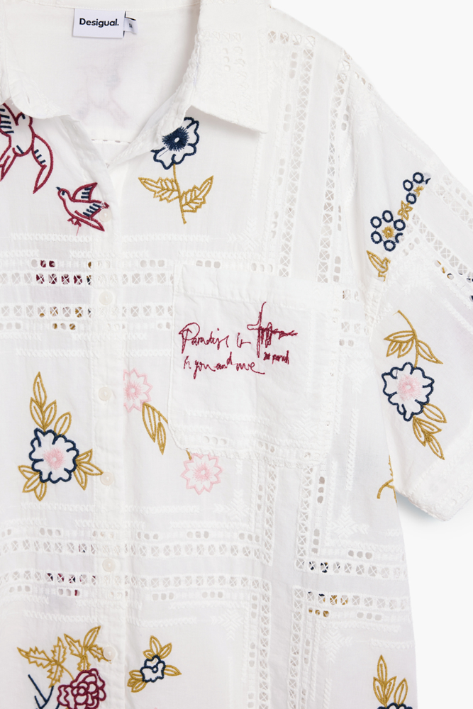 White short-sleeve embroidered shirt by Desigual with eyelet lace panels and multicolor floral and bird motifs in pink, blue, and gold.