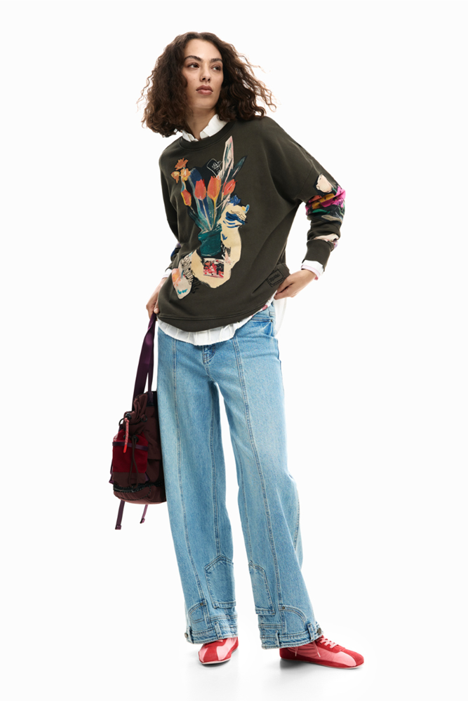 Woman wearing a dark sweater with colorful designs, blue jeans, and red shoes on a white background