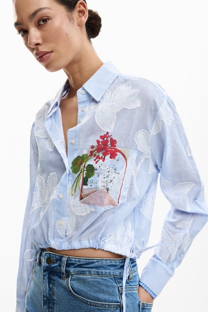 Woman wearing a light blue floral embroidered shirt with a white background