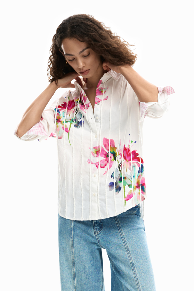 Woman wearing a white blouse with colorful floral patterns and blue jeans on a white background