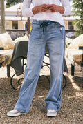 Person wearing light blue jeans standing outdoors with tables and chairs in the background