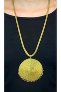 Gold necklace with a large round pendant on a black background