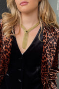 A close-up of a woman wearing a gold mesh Y-necklace with a central black bead, styled over a black velvet top and a leopard-print velvet blazer.