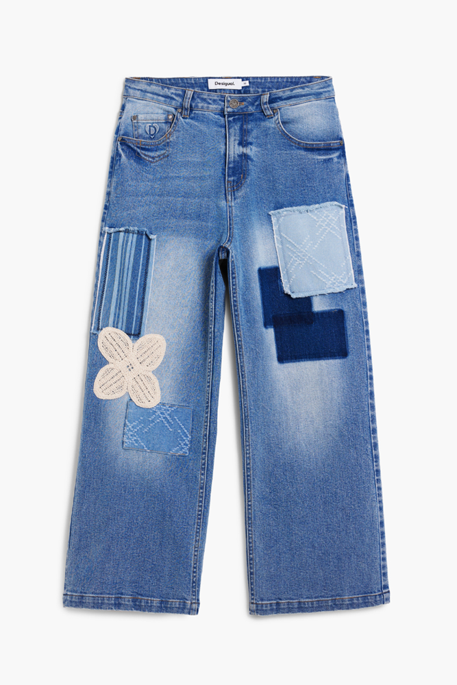 Light blue denim jeans with a straight-leg fit, featuring a large cream crochet flower patch on the right thigh, a striped patch on the upper left leg, and a dark blue geometric patch on the left thigh.