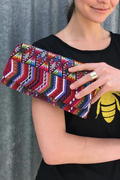 Person holding a colorful patterned clutch against a gray background