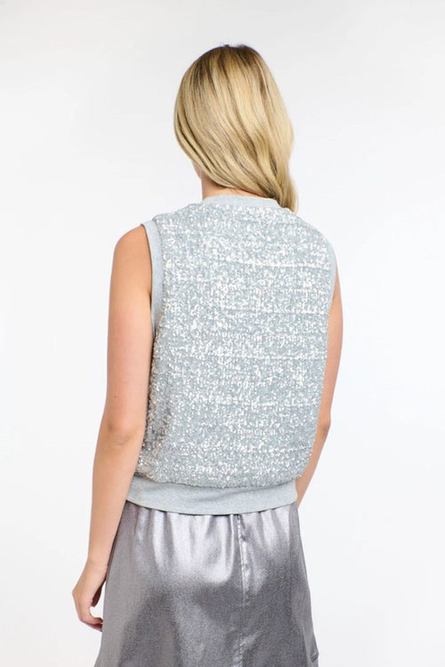 A woman shown from the back wearing a sleeveless textured silver vest and a shiny silver skirt against a plain white studio background.