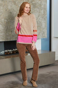 Woman wearing a beige sweater with pink accents and brown pants in an indoor setting.