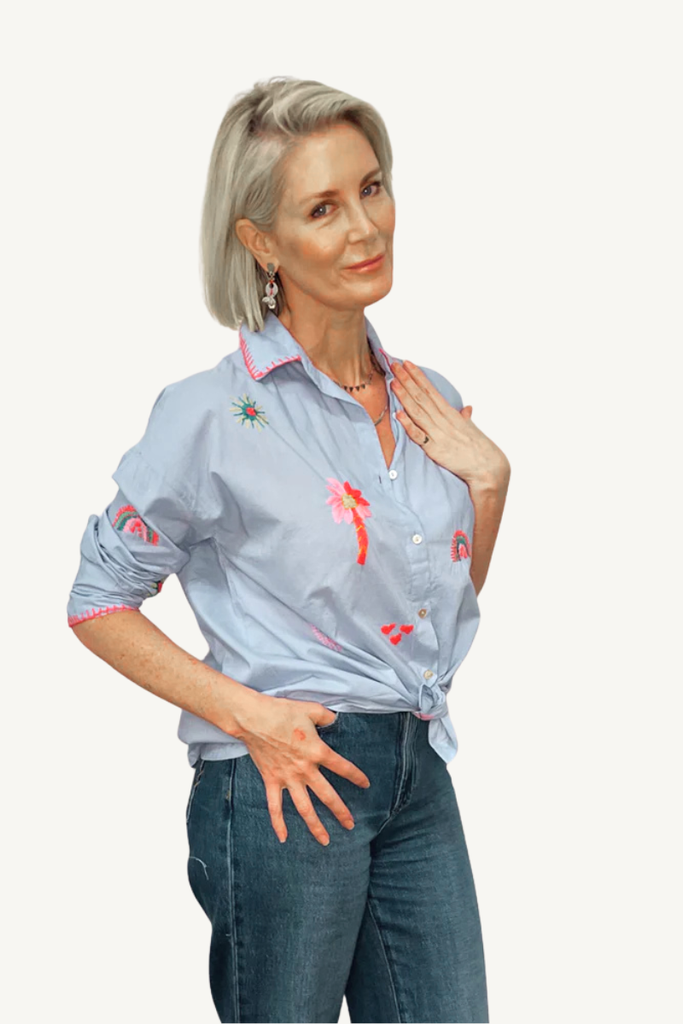 Woman wearing a light blue blouse with floral embroidery and jeans on a white background