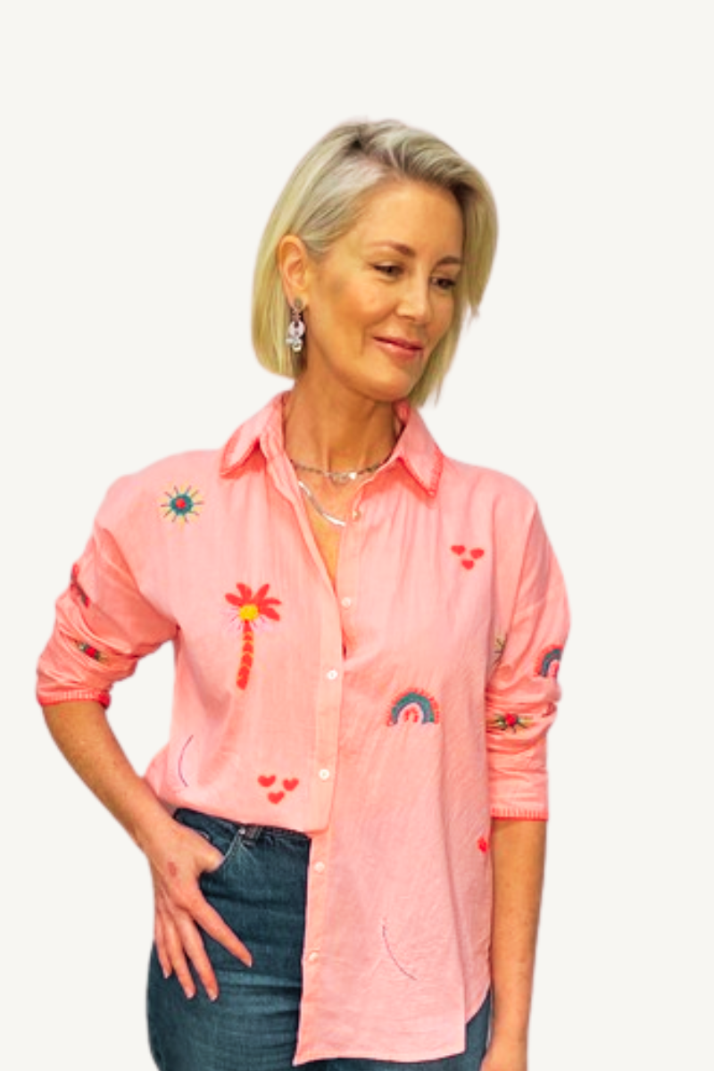 Woman wearing a pink shirt with colorful embroidery on a white background