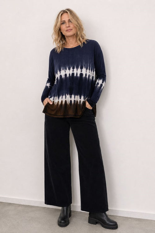 Person wearing a navy and white tie-dye sweater with black pants against a white wall.
