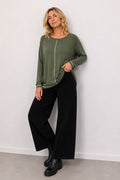 Woman wearing a green top and black pants against a white wall