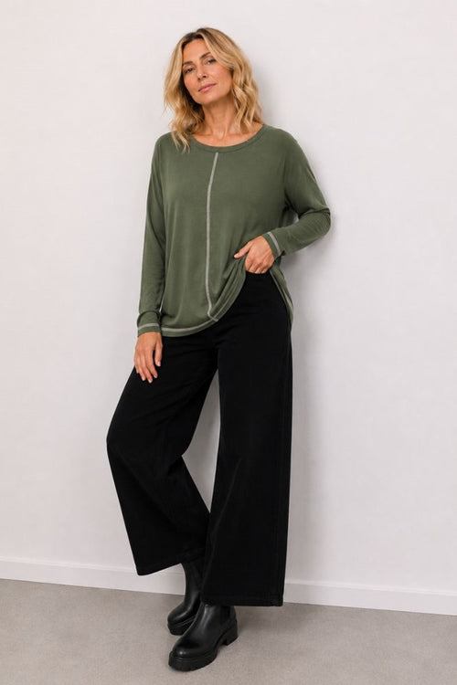 Woman wearing a green top and black pants against a white wall