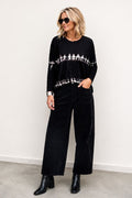 Woman wearing a black tie-dye sweater and black pants against a white background