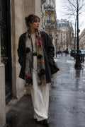 Woman standing on a city street wearing a coat, scarf, and white pants.