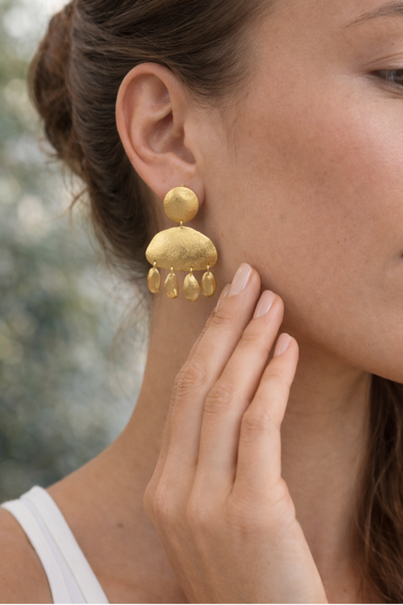 Close-up of a person wearing gold earrings with a blurred natural background