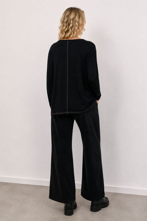 Person wearing a black outfit with wide-leg pants against a white wall