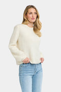 Woman wearing a cream sweater and light blue jeans on a white background