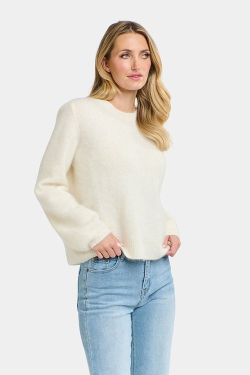 Woman wearing a cream sweater and light blue jeans on a white background