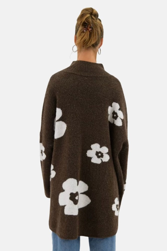 Brown cardigan with white floral patterns worn by a person on a light gray background