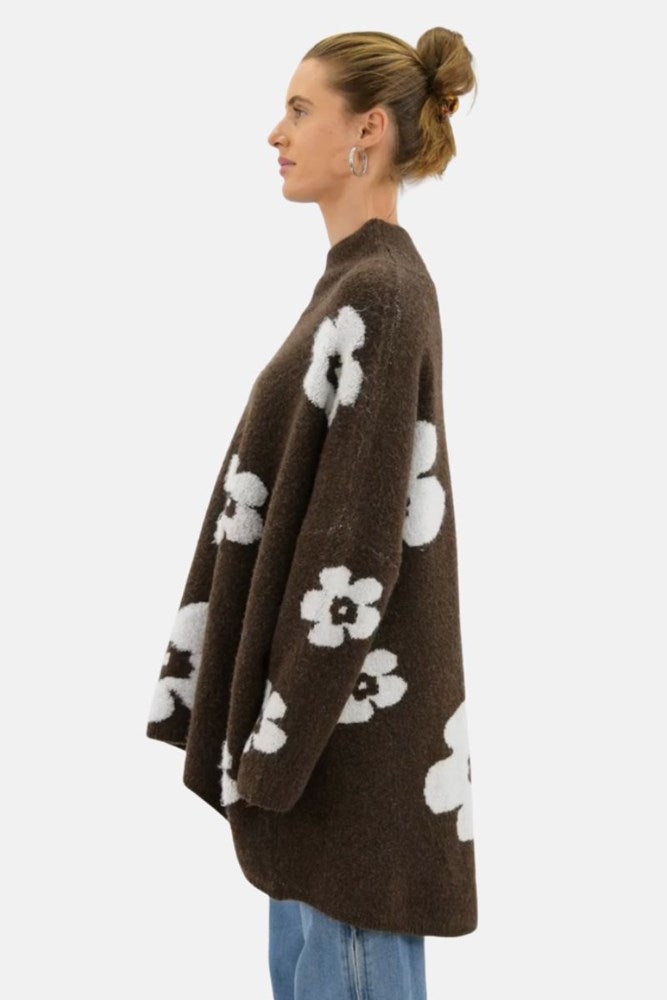 Woman wearing a brown cardigan with white floral patterns on a white background