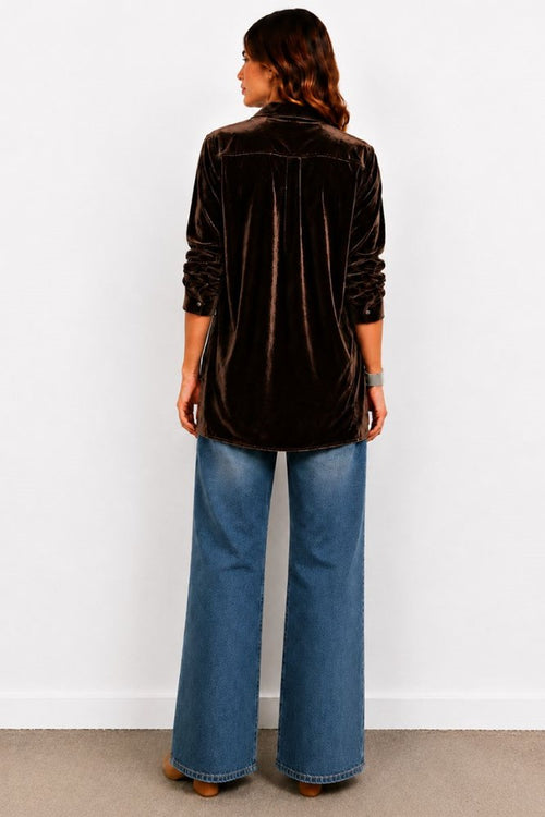 Person wearing a black velvet shirt and blue jeans against a white wall