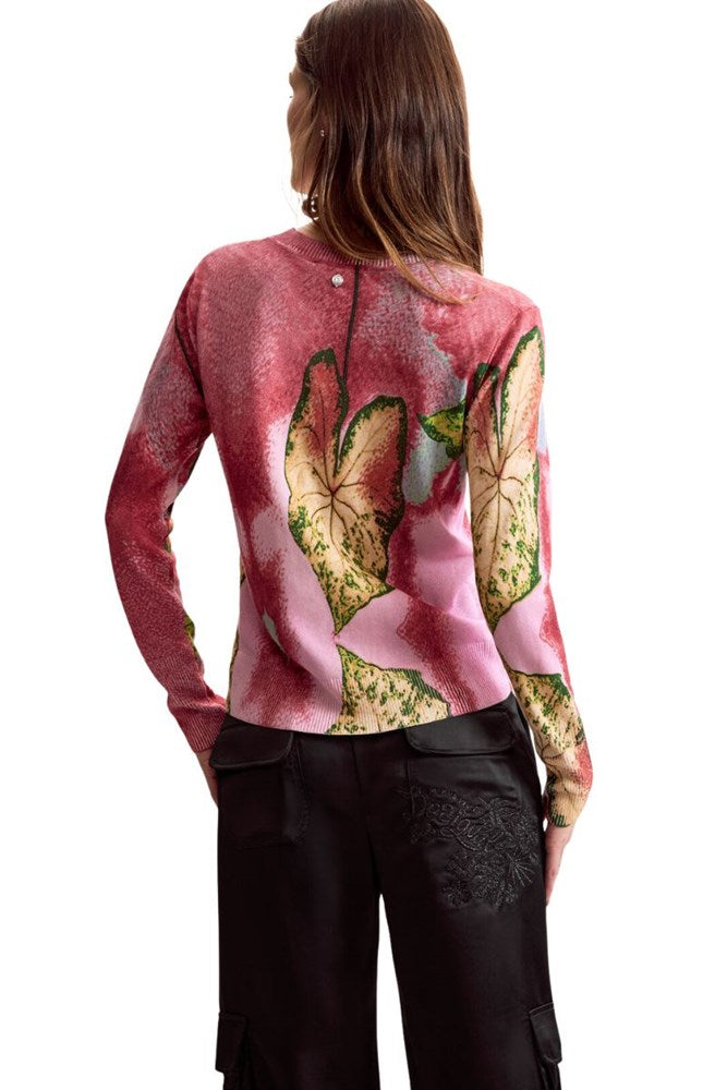 A woman shown from the back wearing a long-sleeve pink top with a large floral print in beige, green, and blue, paired with black pants, against a plain white background.