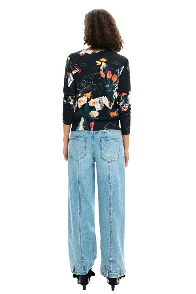A model viewed from the back wearing a black long-sleeve top with a vibrant multicolor floral print and light-wash wide-leg jeans.