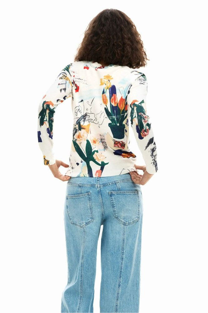 A woman viewed from behind wearing a long-sleeve white top with a colorful botanical and animal print, paired with light blue jeans, against a plain white background.