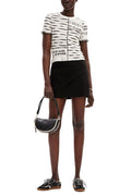 A model wearing a black and white striped short-sleeve top with text graphics, a black wrap-style mini skirt, and black sneakers, holding a black crescent handbag against a plain white background.