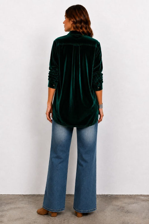 Person wearing a green velvet shirt and blue jeans against a white background