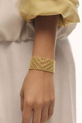 Gold bracelet on a wrist with a neutral background