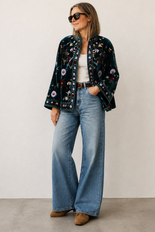 Woman wearing a floral jacket, white top, and blue jeans against a plain background