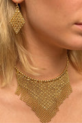 Close-up of a model wearing a chunky gold beaded fringe choker necklace and a matching geometric drop earring.