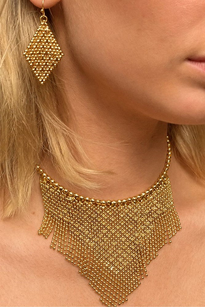 Close-up of a model wearing a chunky gold beaded fringe choker necklace and a matching geometric drop earring.