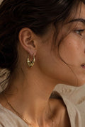 Close-up of a person wearing gold hoop earrings with a neutral background