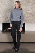 Woman wearing a gray sweater and black jeans standing in front of a stone fireplace.