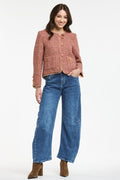 A woman modeling a cropped, textured dusty rose tweed jacket with gold buttons, paired with wide-leg blue jeans and brown ankle boots, against a plain white studio background.