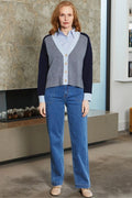 Woman wearing a navy sweater vest over a light blue shirt with a white collar, paired with blue jeans, standing indoors.