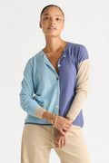 A model wearing a color-blocked cardigan with light blue, lavender purple, and beige panels, paired with beige pants, against a plain white studio background.
