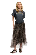 A woman modeling a dark gray graphic t-shirt and a sheer leopard-print tulle midi skirt with a black-and-white leopard print overlay, paired with black sneakers, against a plain white background.