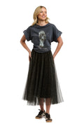 A woman modeling a dark gray graphic t-shirt and a long black tulle midi skirt with a subtle pattern, paired with brown sneakers, against a plain white background.