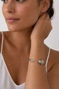 A close-up lifestyle shot of a woman wearing a silver-toned metal cuff bracelet with a polished snake head charm on her wrist.