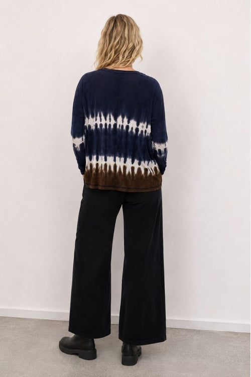 Person wearing a tie-dye sweater and black pants against a white background