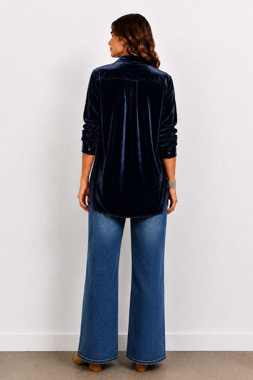 Person wearing a dark blue velvet shirt and blue jeans against a white background