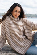 Woman wearing a striped sweater sitting by a body of water.