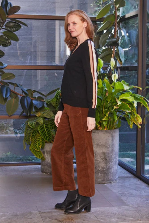 Woman in black top and brown pants standing in a modern indoor setting with plants.
